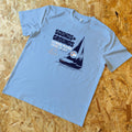 Light blue t-shirt with sailboat graphic and text on a wooden surface